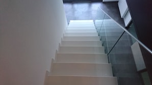Una scala moderna con ringhiere in vetro e gradini bianchi che conducono a un piano superiore.