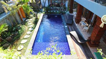 A rectangular swimming pool with a clear blue water surface, surrounded by a garden with various plants and a wooden deck.