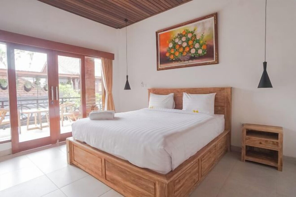 Une chambre avec un lit en bois, un tableau et une vue sur l’extérieur, accessible par une porte coulissante qui donne sur un espace extérieur.