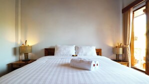 A neatly made bed with white linens and a rolled towel, two pillows, and two bedside tables with lamps. - Pondok DD Canggu (Canggu)