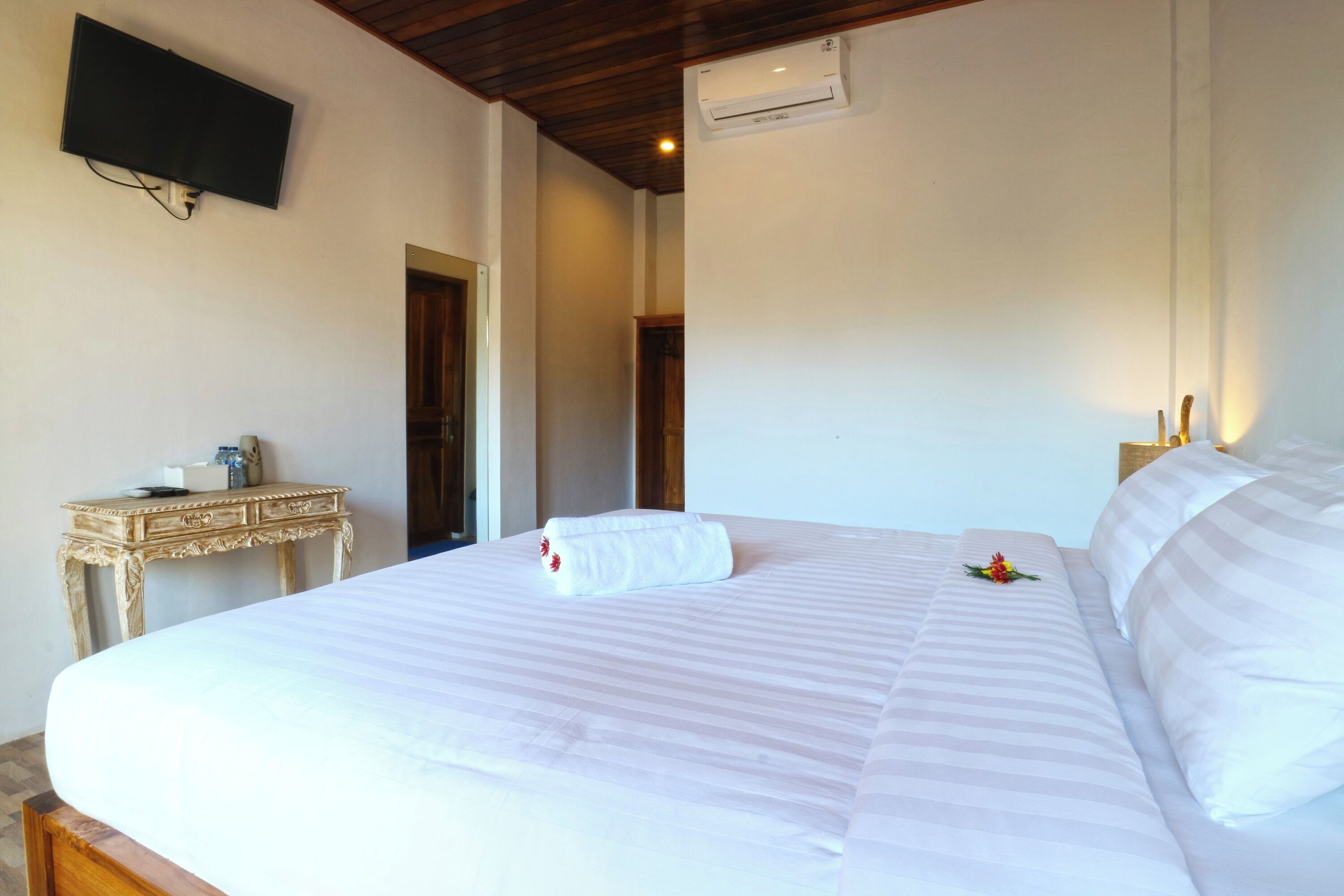 Quarto de hotel com uma cama grande, uma mesa pequena, uma televisão na parede e um aparelho de ar condicionado.