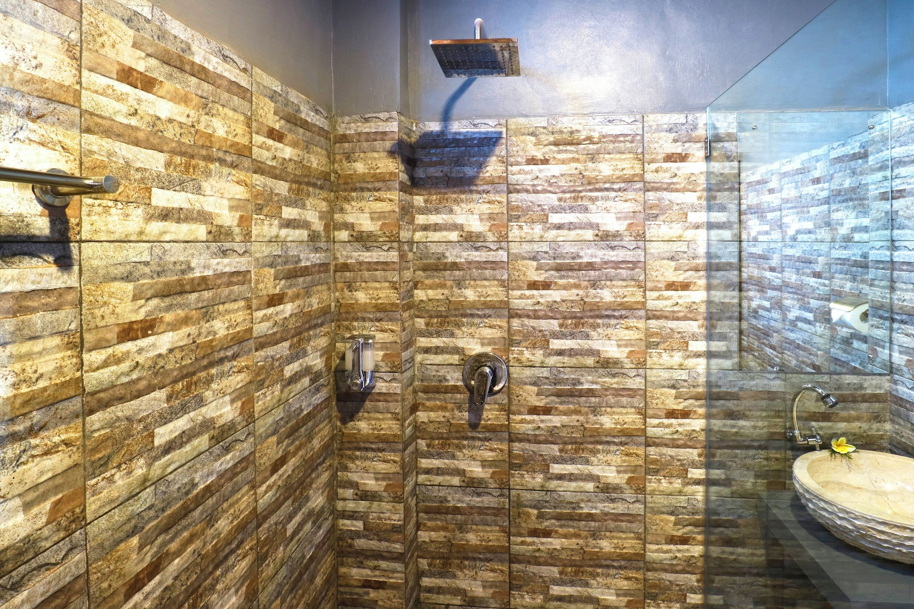 Un baño con ducha de pared de piedra, lavamanos con estructura de vidrio y ducha de mano.