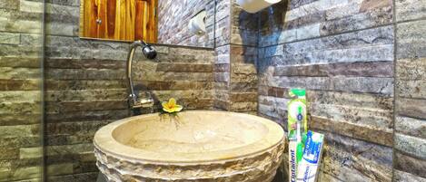 A bathroom with a stone sink, a mirror, a toilet paper holder, and a hand soap dispenser.