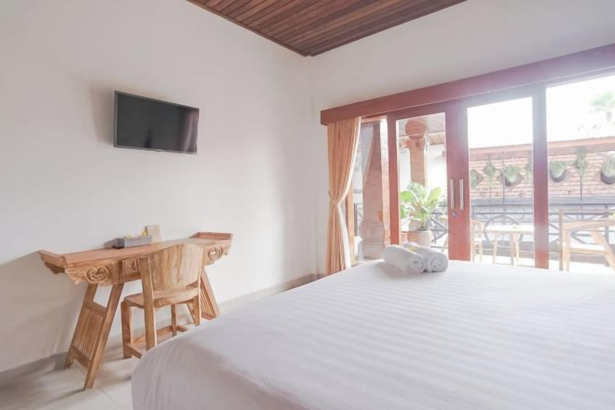 Une chambre avec un lit, un bureau, une télévision et un balcon agrémenté de plantes.