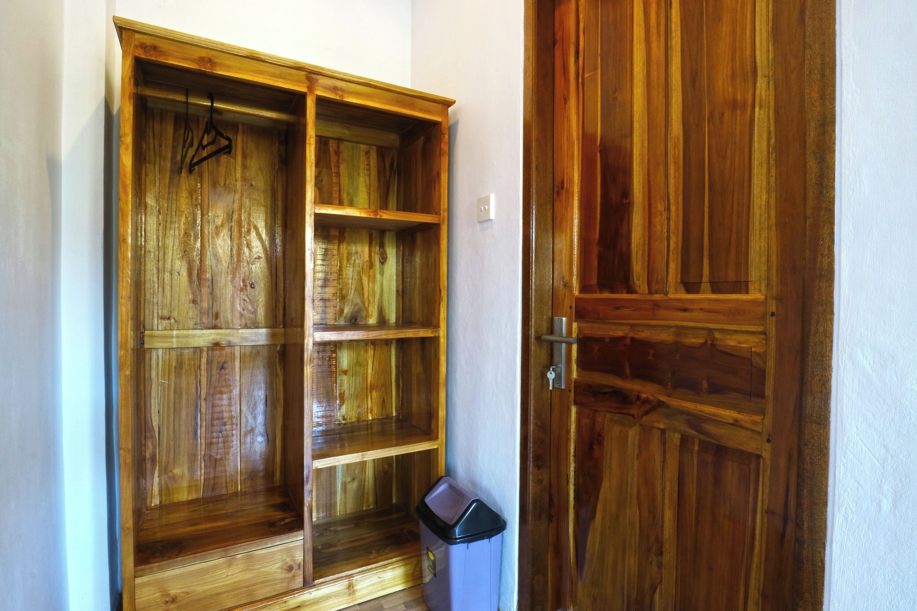 Une armoire en bois avec plusieurs étagères et une tringle pour suspendre les vêtements, une poubelle et une porte en bois.