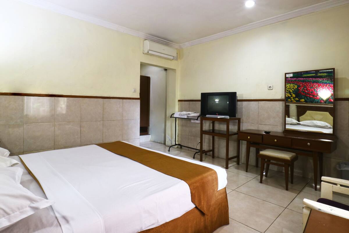 Une chambre d’hôtel avec un grand lit, un bureau avec une chaise, une télévision et un miroir.