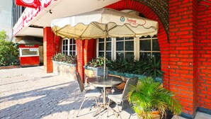 A hotel exterior with a red brick facade, a covered outdoor seating area with a table and chairs, and a sign indicating the hotel name. - Hotel Tanjung (Surabaya)