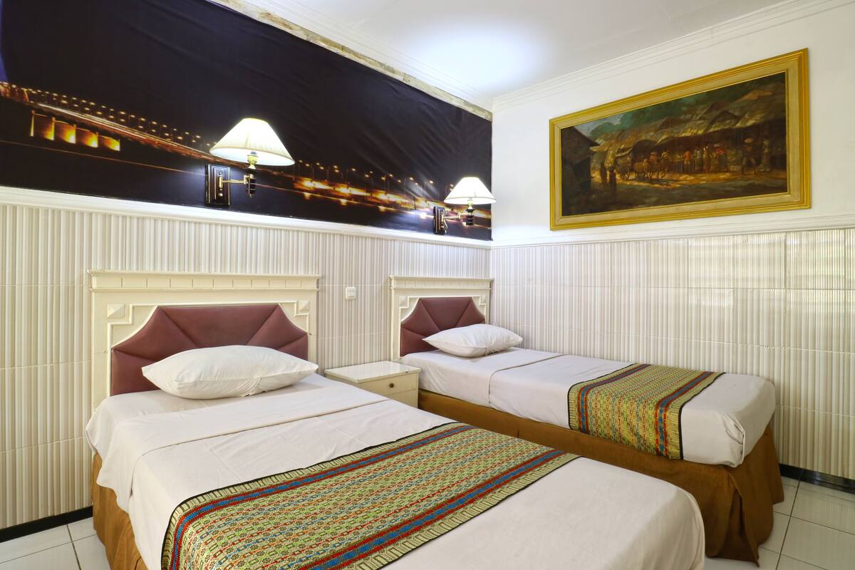 Une chambre d’hôtel avec deux lits, un grand tableau au mur et une fresque représentant un paysage nocturne au-dessus des lits.
