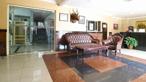 A lobby with a glass door entrance, a brown leather sofa, a wooden coffee table, and a mounted deer head. - Hotel Tanjung (Surabaya)