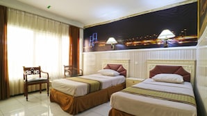 A hotel room with two beds, a chair, and a large window with curtains. - Hotel Tanjung (Surabaya)