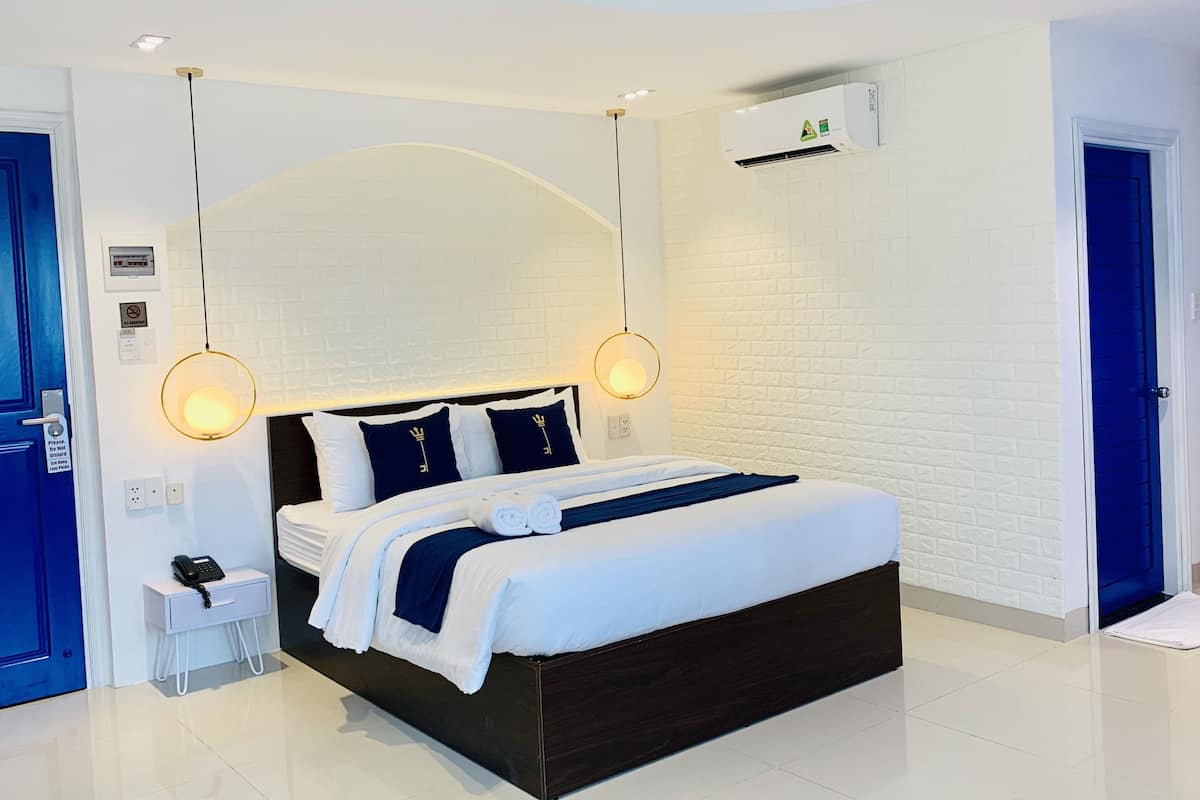 A modern hotel room with a large bed, white brick walls, and a blue door.