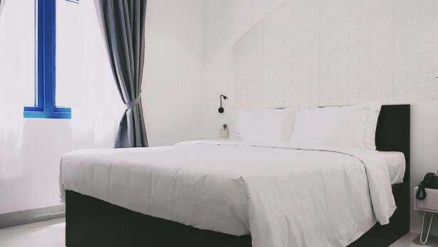A modern bedroom with a large bed, white bedding, a black headboard, a bedside table with a lamp, and a window with curtains.