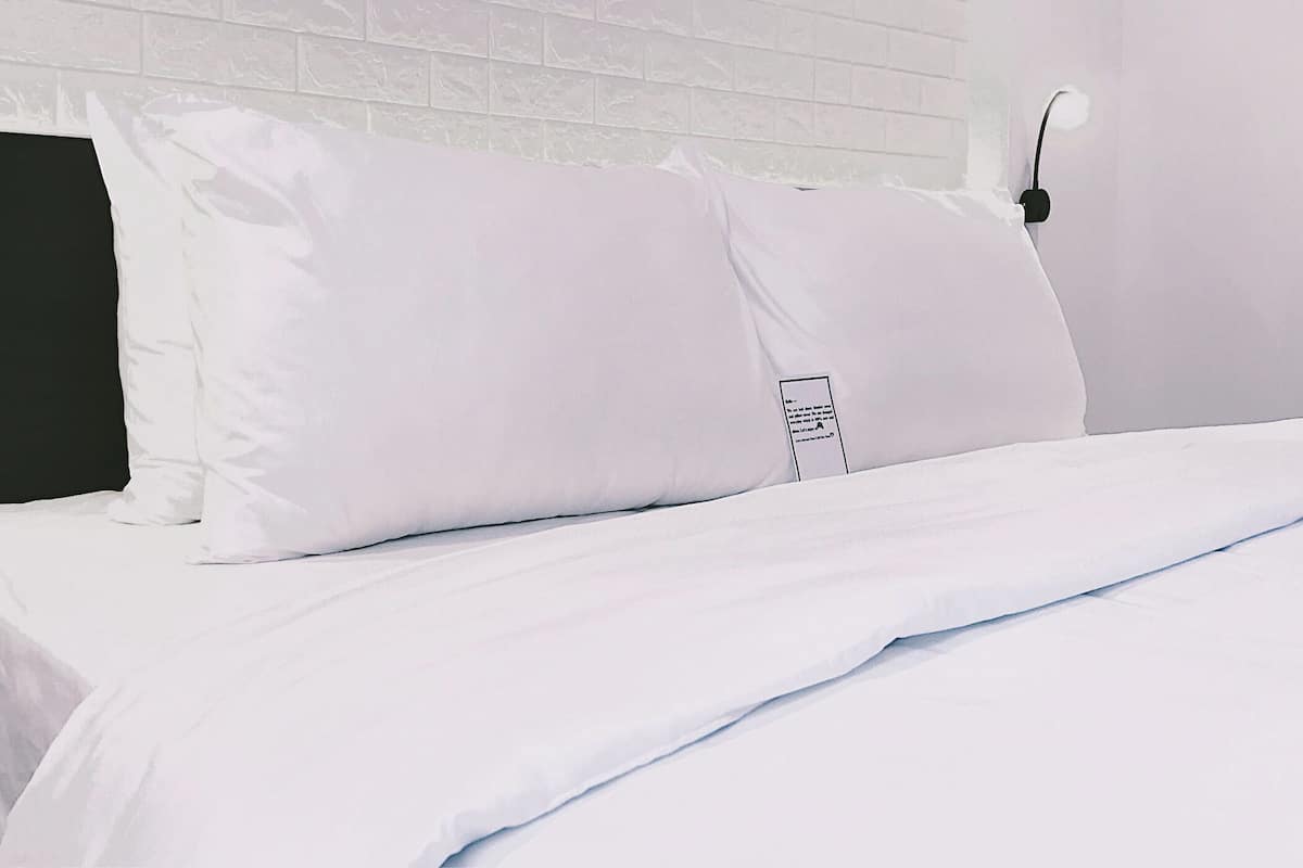 A neatly made bed with white bedding and pillows, a black headboard, and a white brick wall.