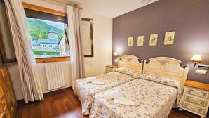 A double room with two beds, a window with curtains, a radiator, a wooden dresser, and a wall with four framed pictures. - Apartamentos Gavín Biescas 3000 (Biescas)