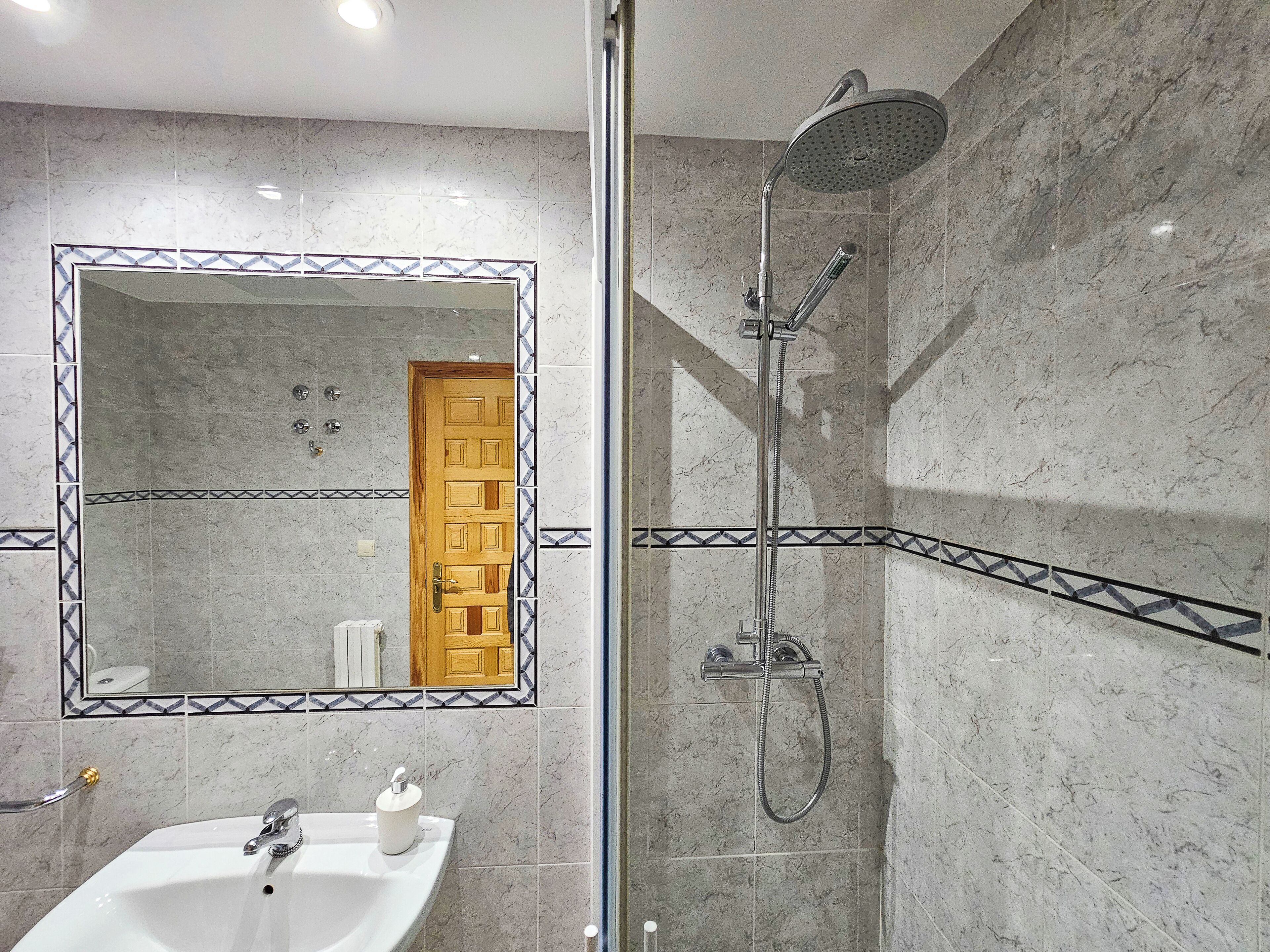 A bathroom with a marble-tiled shower, a sink with a mirror, and a wooden door.