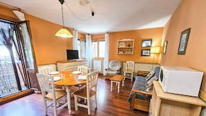 A cozy living room with a dining area, wooden furniture, a television, and a microwave. - Apartamentos Gavín Biescas 3000 (Biescas)