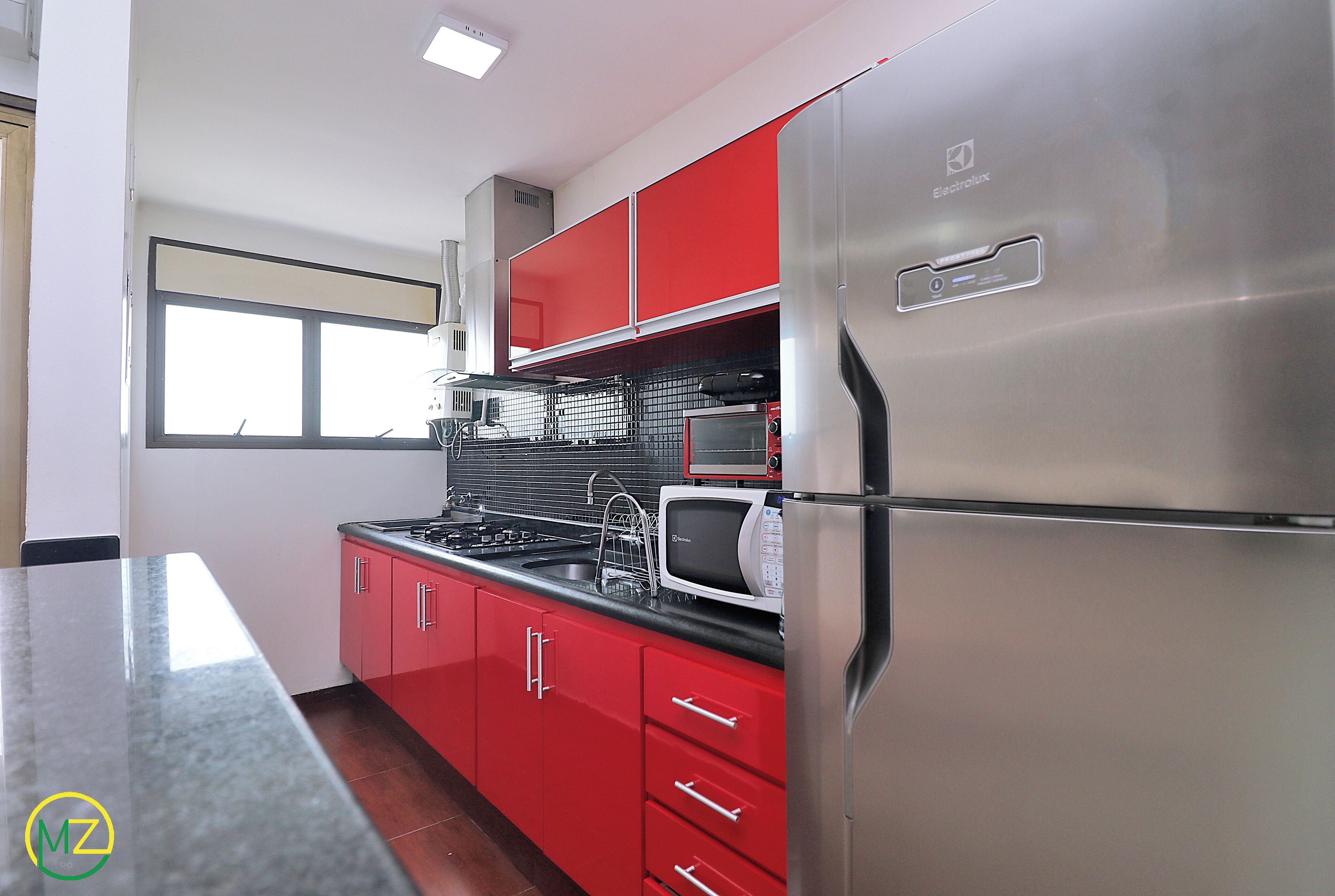 A kitchen with red cabinets, a stainless steel refrigerator, a microwave, and a stove.