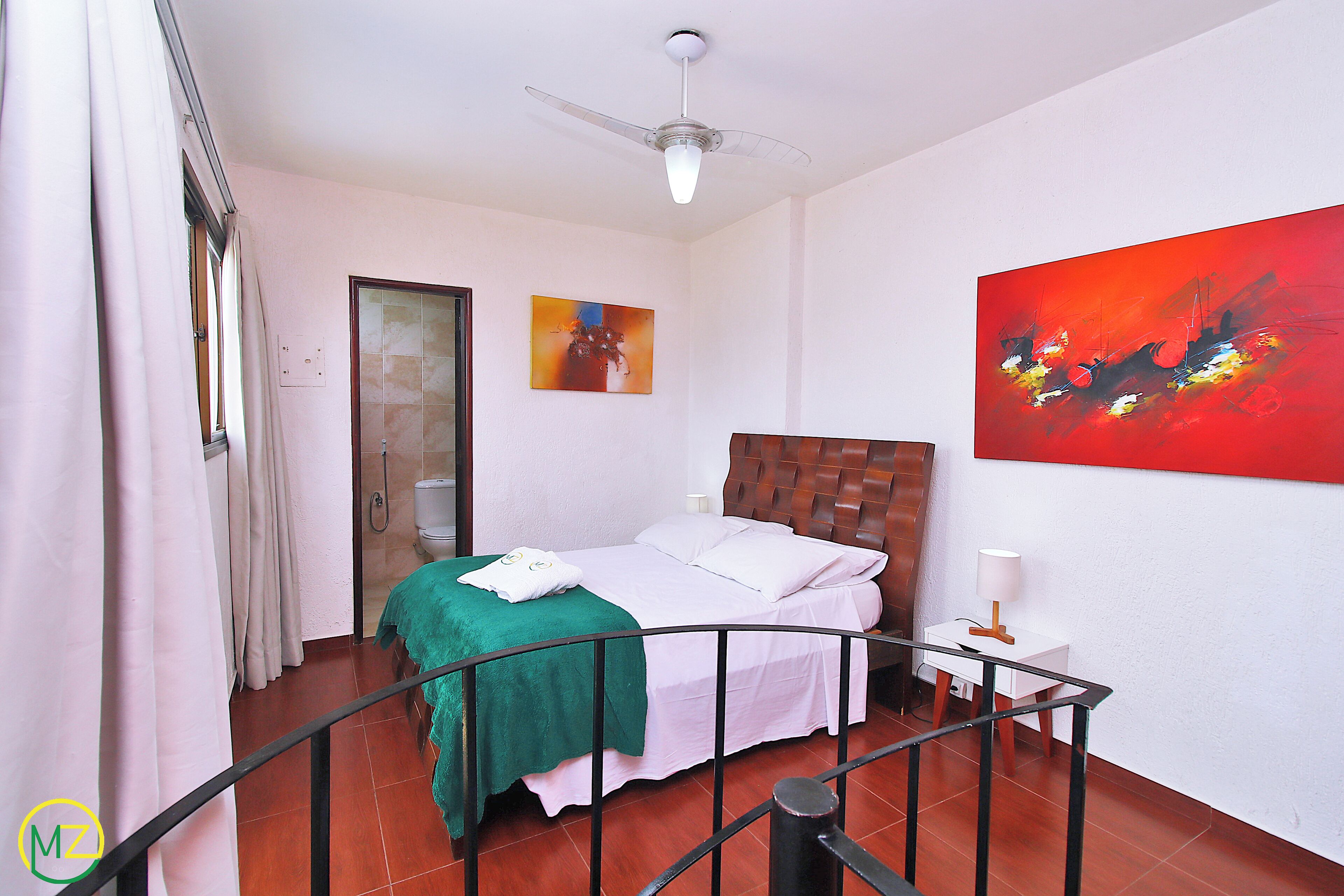A bedroom with a bed, a ceiling fan, a painting, and a nightstand.