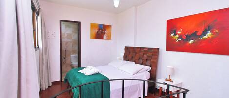 A bedroom with a bed, a ceiling fan, a painting, and a nightstand.