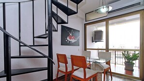 A dining area with a glass table, two wooden chairs, a black and white painting, and a view through a large window. - MZapartments Raul Penthouse 06 (Rio de Janeiro)