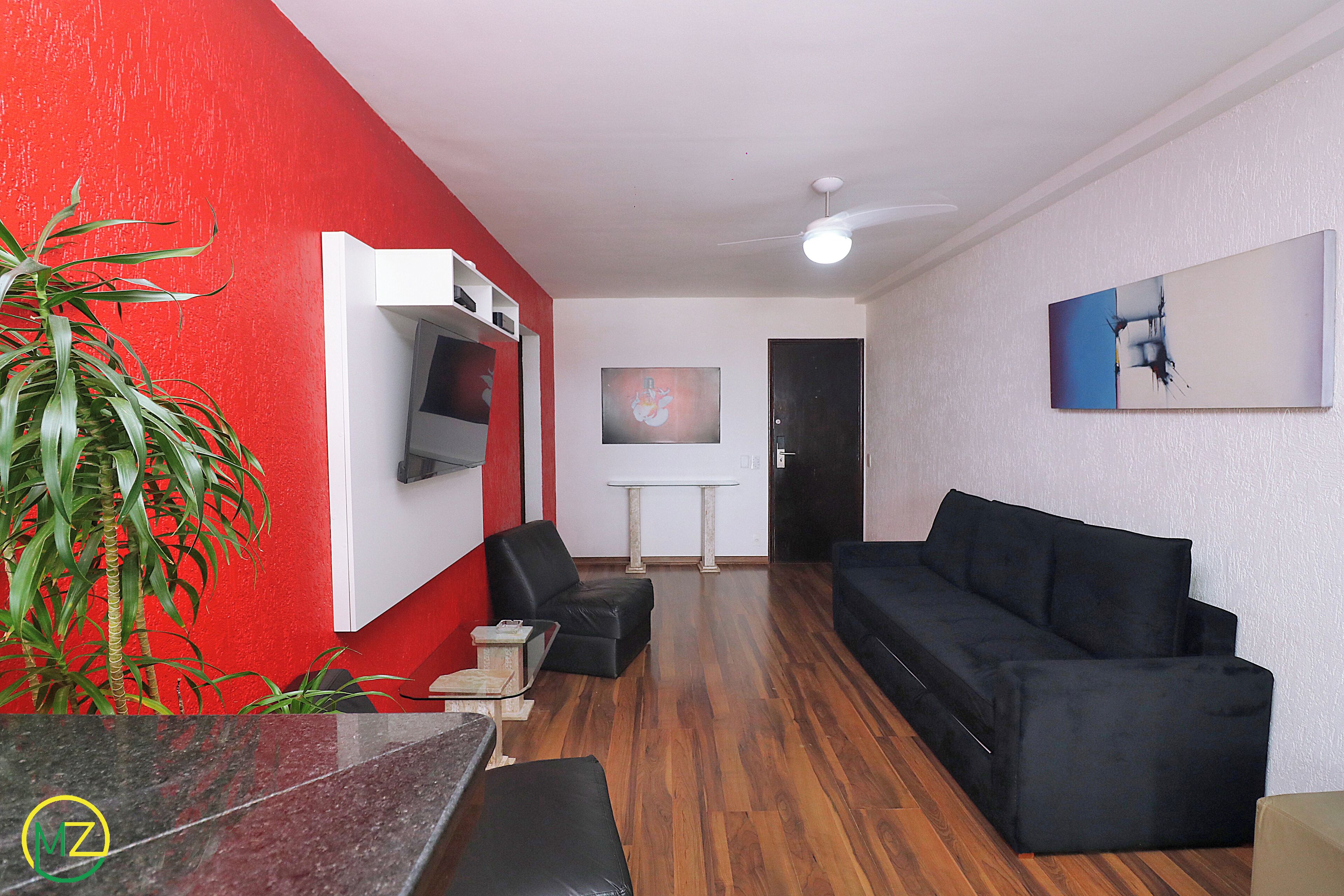 Ein Wohnzimmer mit roter Wand, einer schwarzen Couch, einem weißen Tisch und einem Deckenventilator.