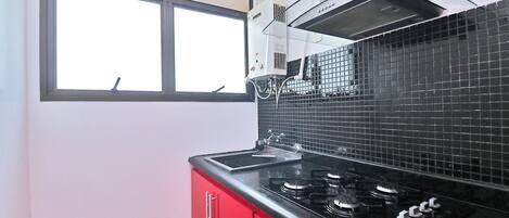 A kitchen with a black tiled backsplash, a window, and red cabinets.