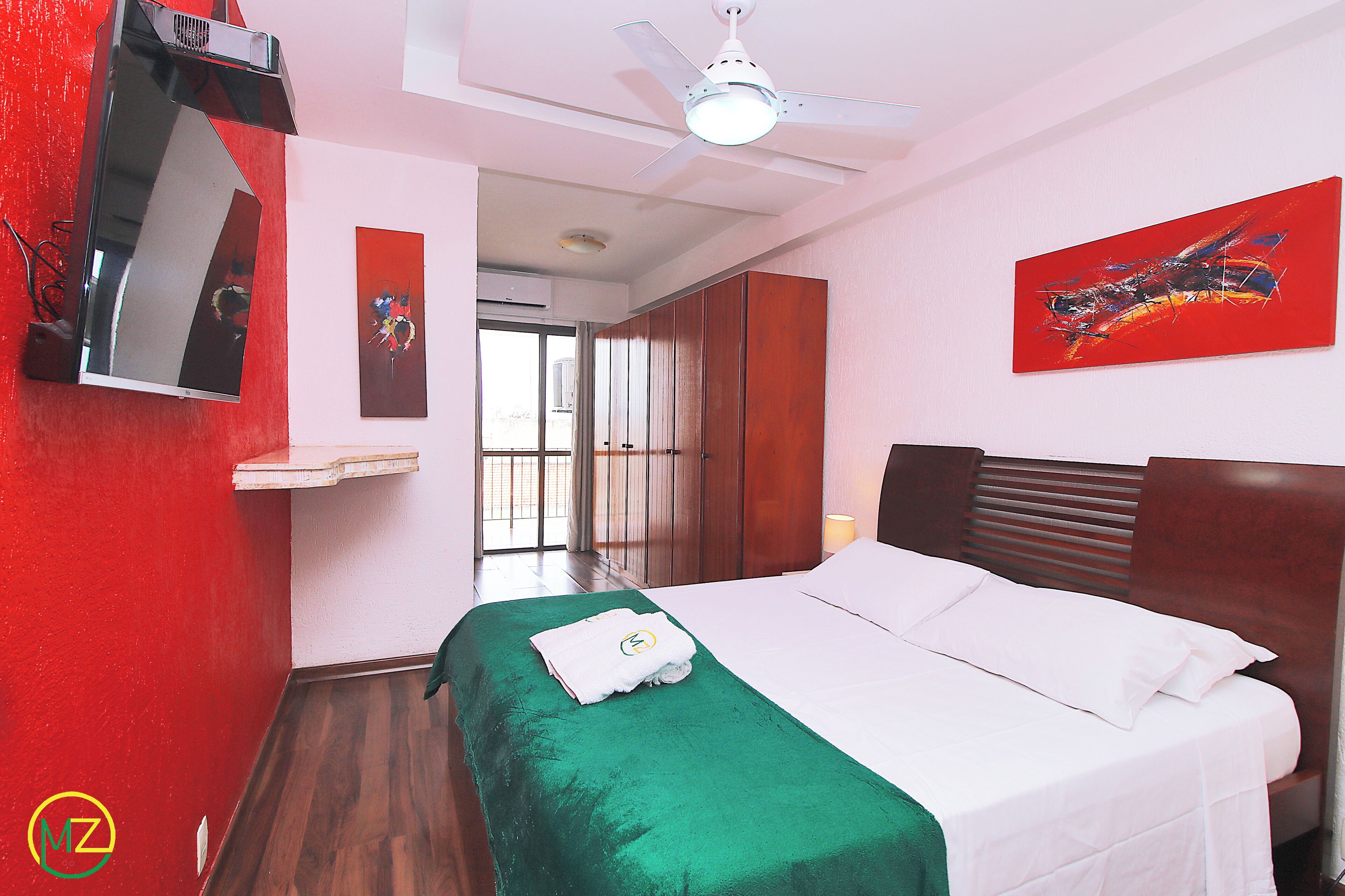 A hotel room with a bed, a ceiling fan, a painting, and a window.