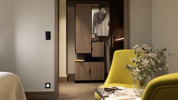 Habitació d'hotel moderna amb un armari de fusta, un otomà groc, una taula petita amb un ram de flors i una revista.