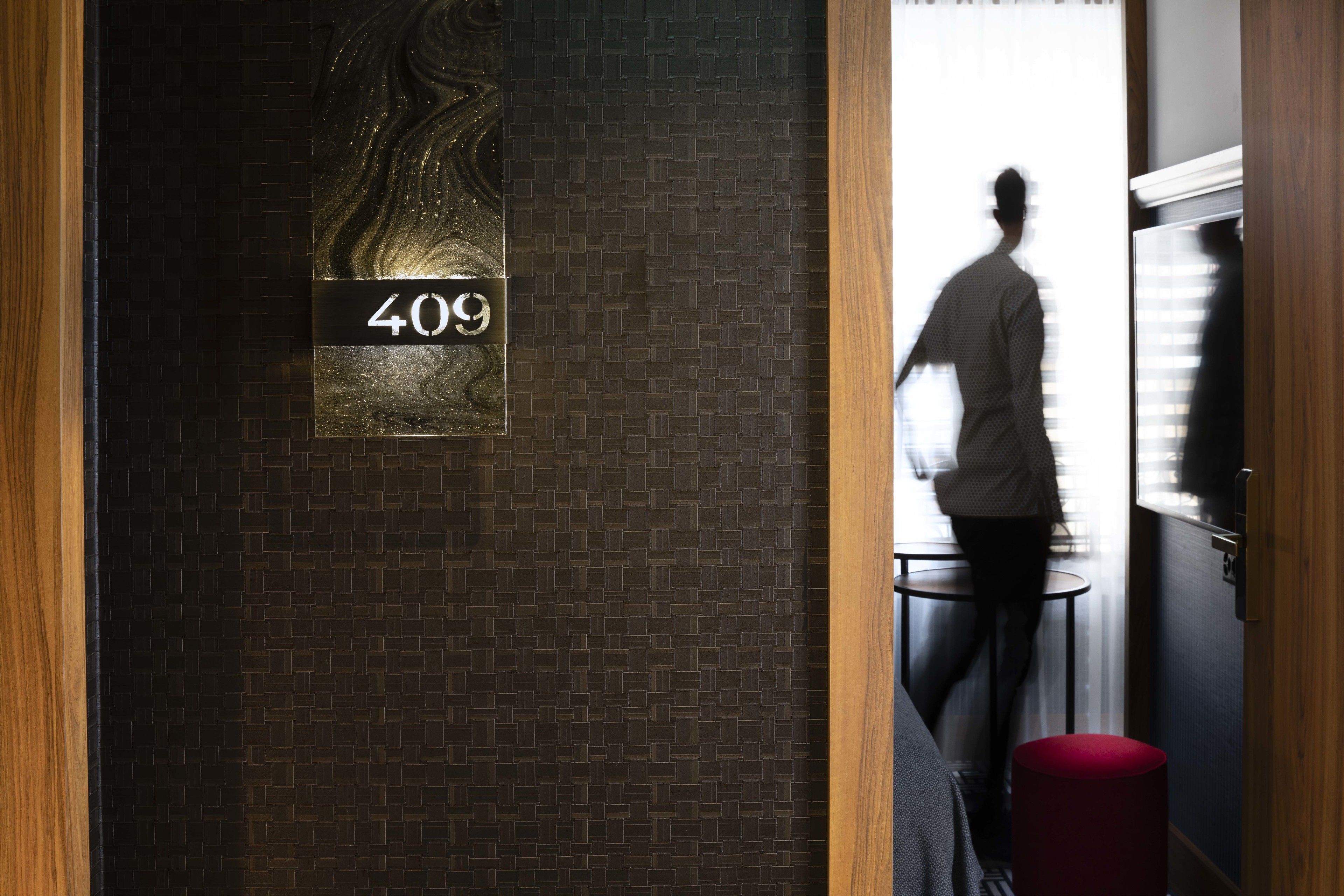 A hotel room with a number sign, a brick wall, a wooden door frame, and a red cylindrical object.