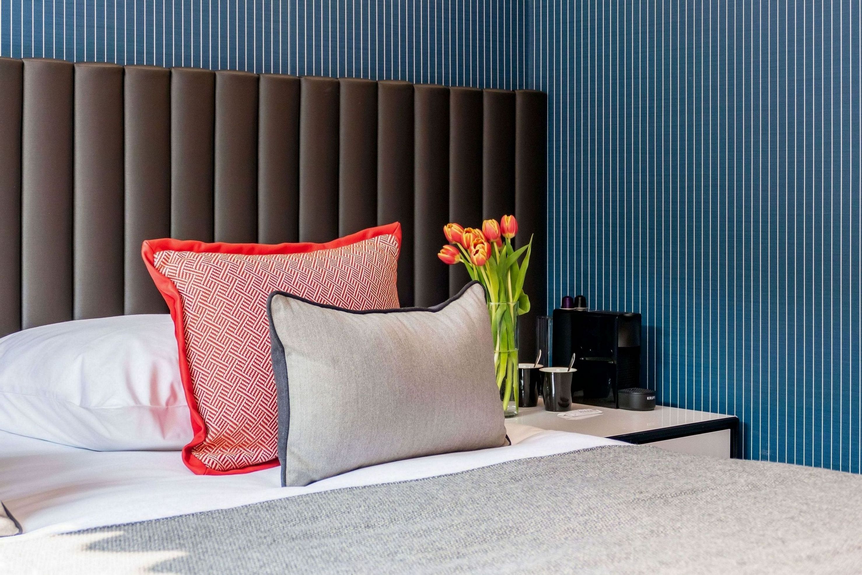 Una habitación de hotel moderna con una cama, una mesita de noche, un jarrón de tulipanes y una pared a rayas.