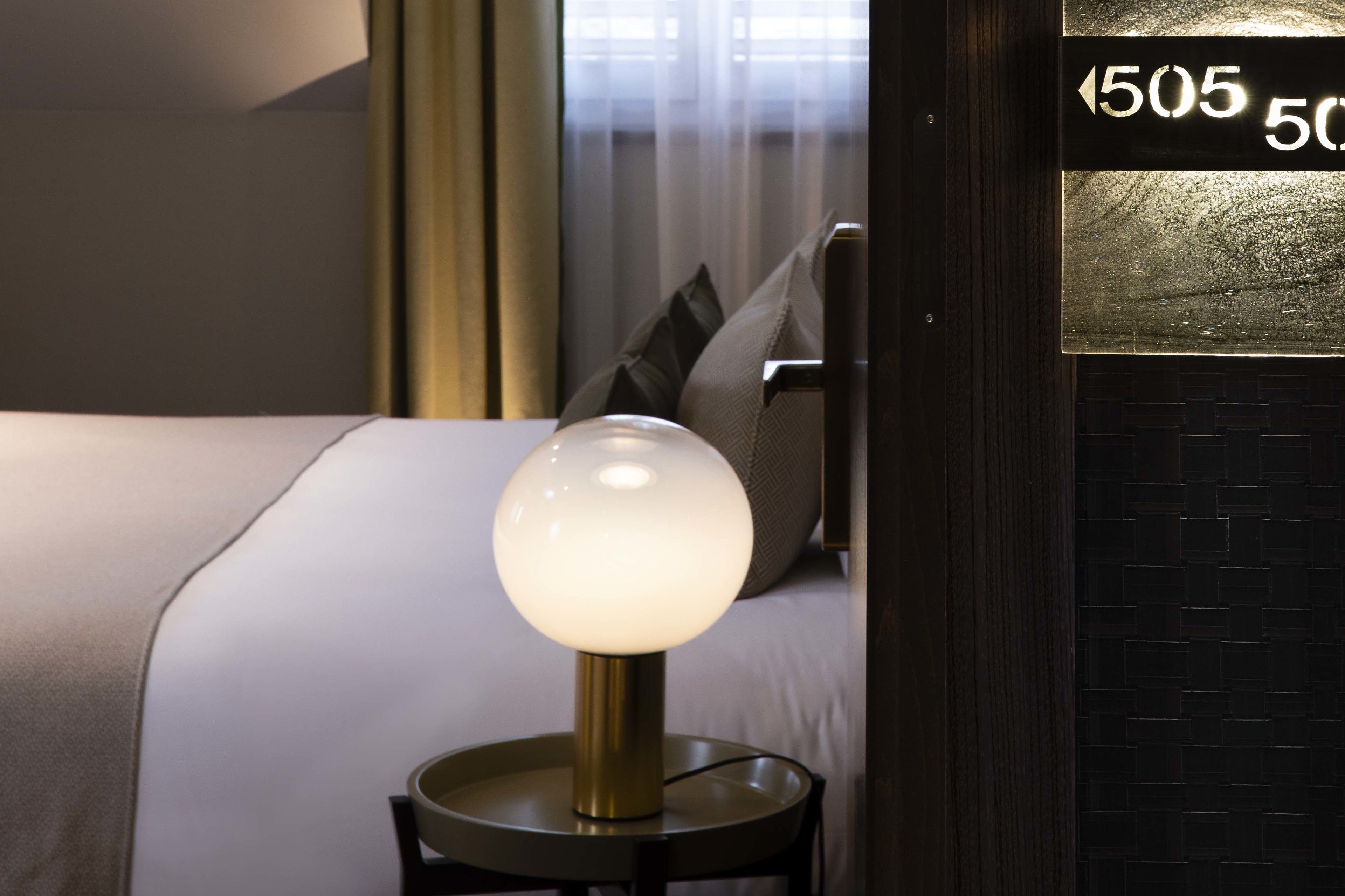 A hotel room with a bed, a round table lamp, a pillow, and a wall-mounted sign with room number 505.