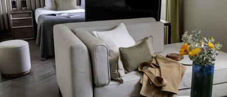 A modern hotel room with a sofa, a coffee table, a TV, and a bed with a headboard.