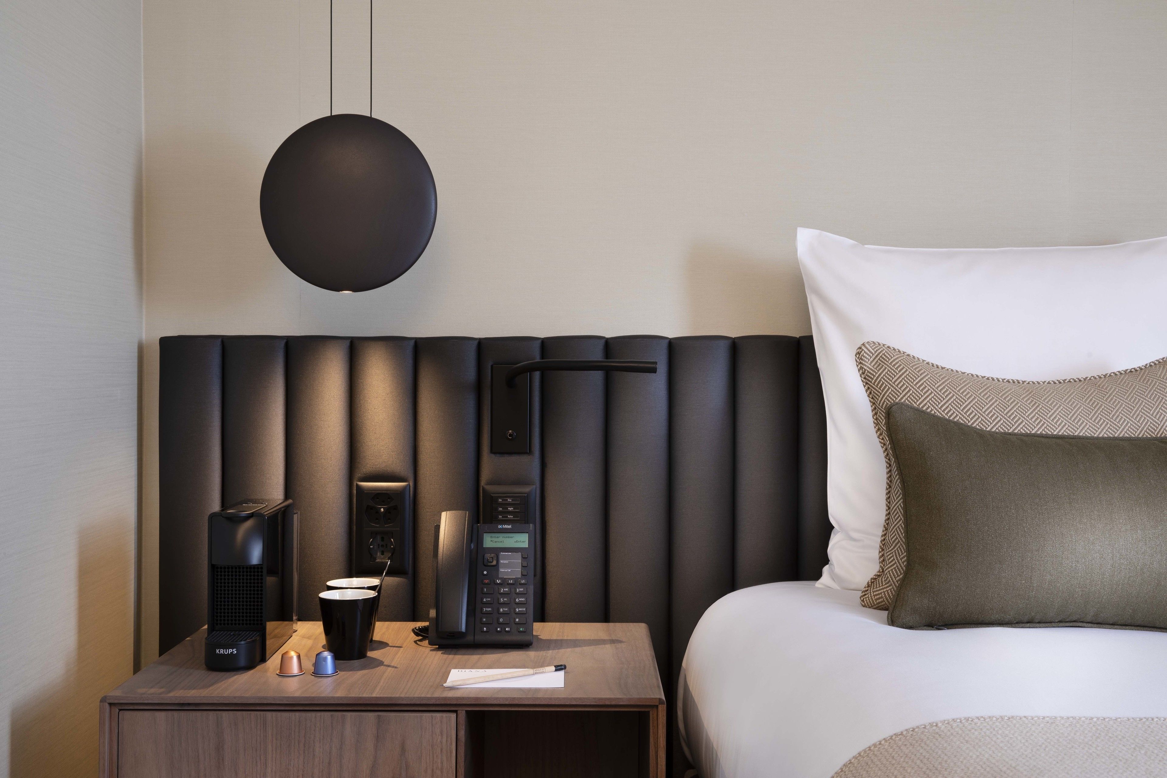 Una habitación de hotel moderna con una cama, una mesita de noche con teléfono, cafetera y lámpara.