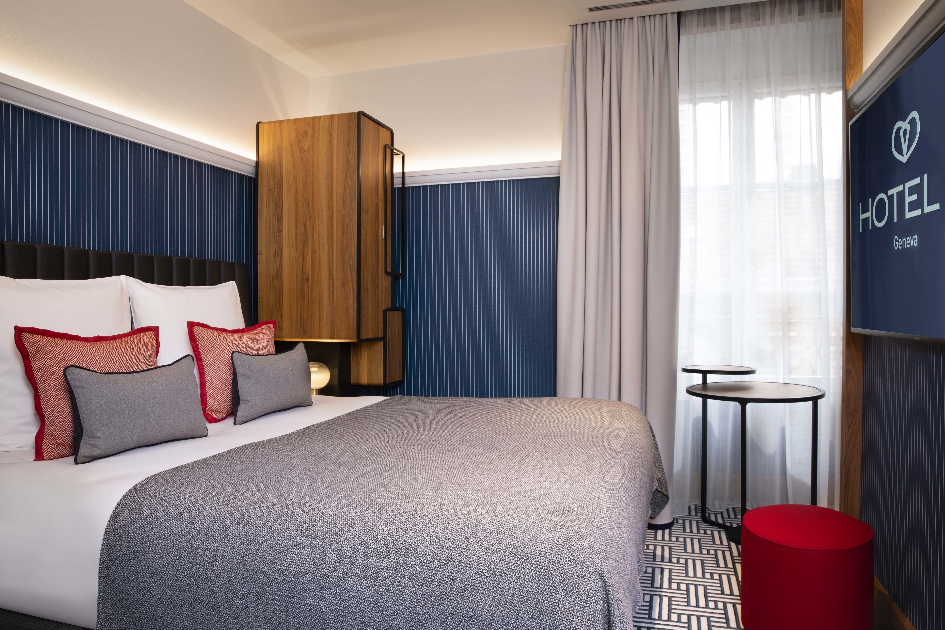 Een hotelkamer met een groot bed, een houten garderobe, een tafeltje en een rode kruk.
