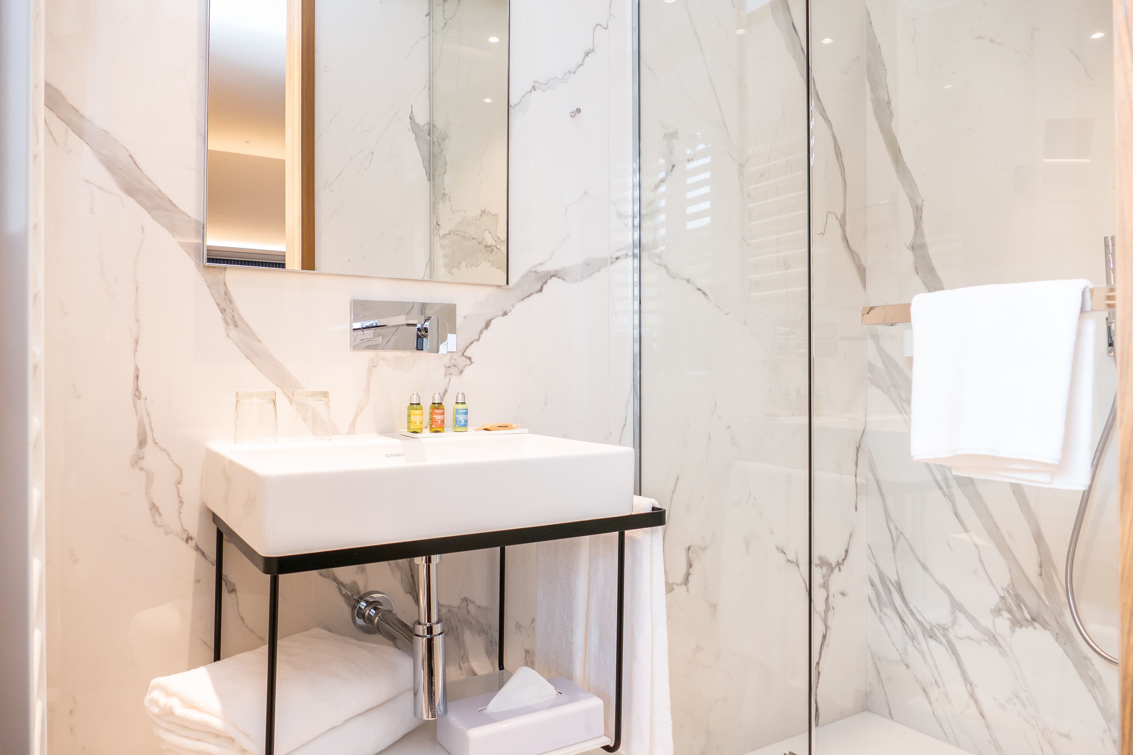 A modern bathroom with a marble sink, a glass shower enclosure, and a towel rack.