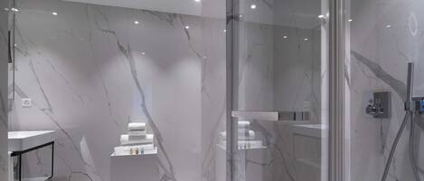 A modern bathroom with marble walls, a glass shower enclosure, and a white pedestal vanity with toiletries.
