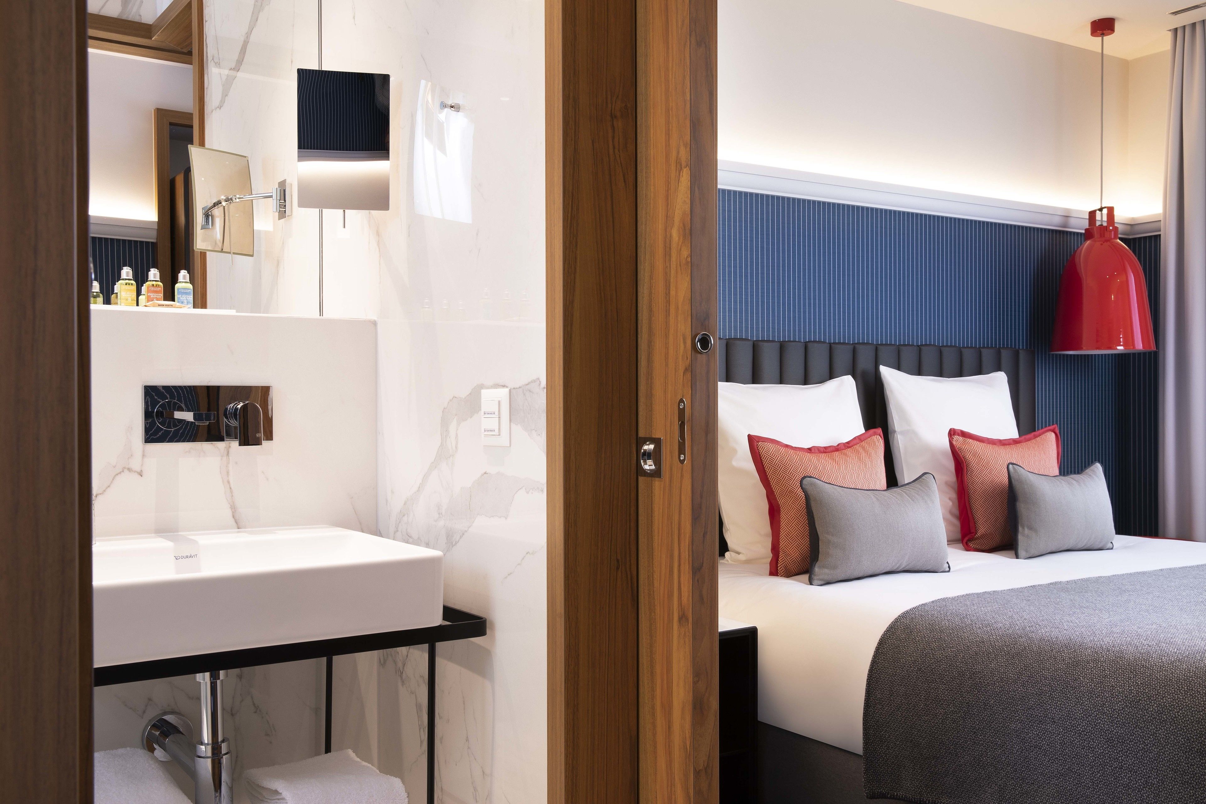 Una habitación de hotel moderna con un lavamanos de mármol, una mesita de noche y una cama con muchas almohadas.