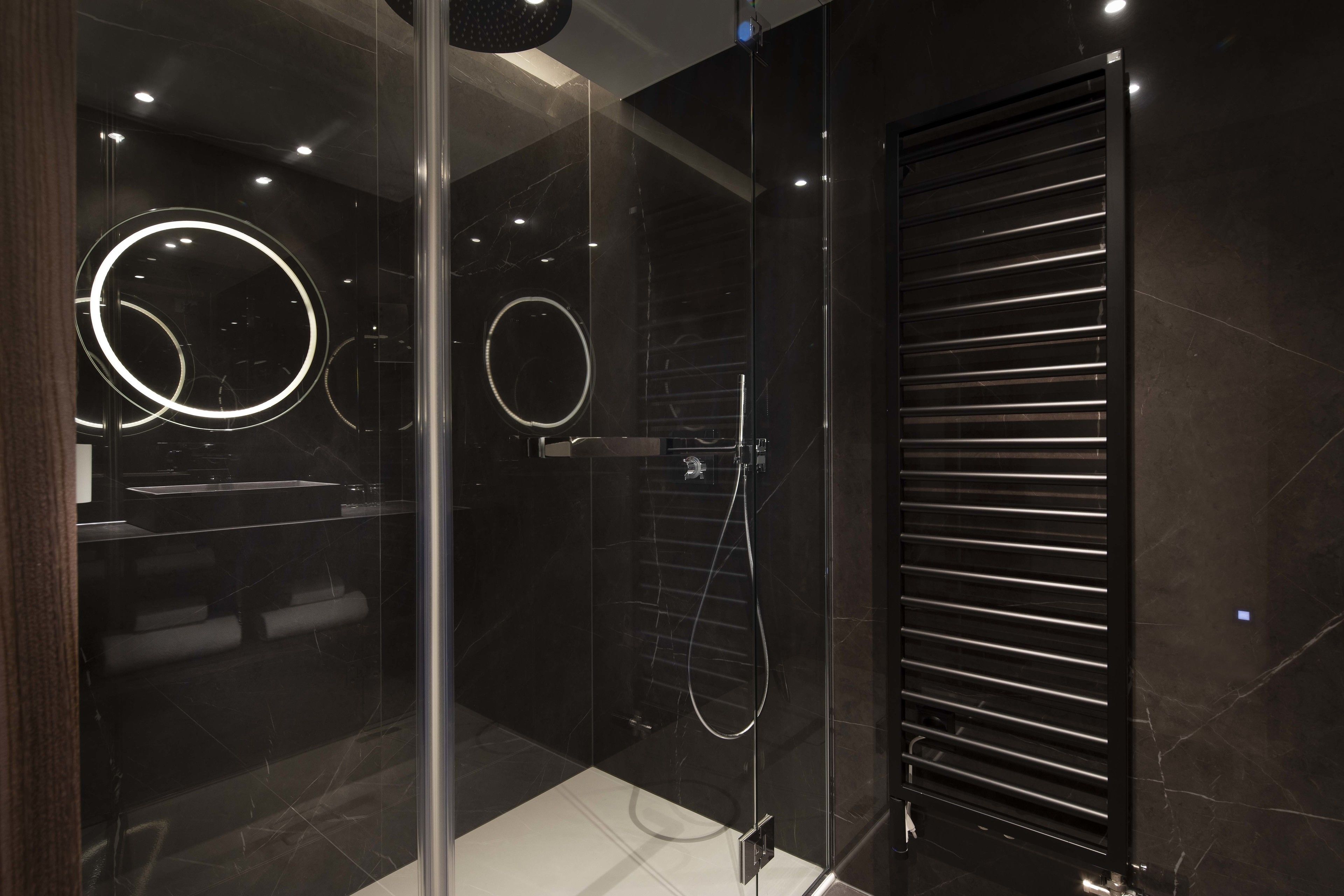 Un bagno moderno con cabina doccia in vetro, parete rivestita in piastrelle nere e lampada a plafoniera circolare.