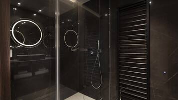 Un bagno moderno con cabina doccia in vetro, parete rivestita in piastrelle nere e lampada a plafoniera circolare.