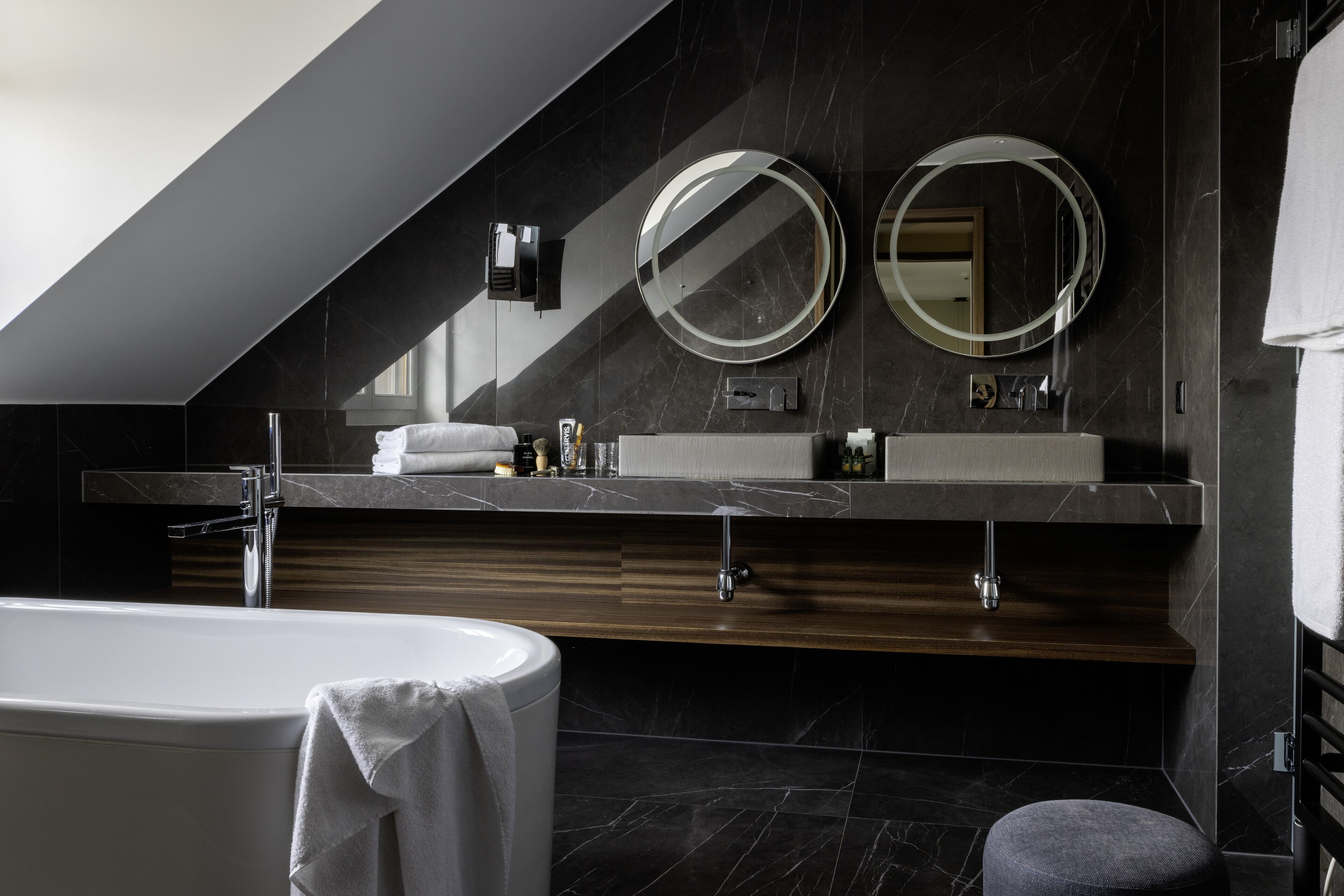 Une salle de bain moderne avec une baignoire sur pieds, deux miroirs fixés au mur et un meuble-lavabo doté d'un plan de travail en marbre foncé.