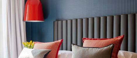 A hotel room with a bed, a red pendant light, and a blue-striped wall.