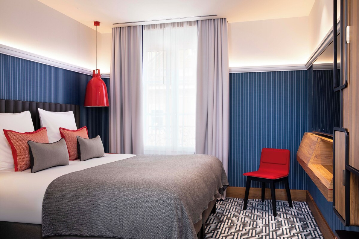 Una habitación de hotel con una cama grande, una silla roja, un armario de madera y un suelo estampado.