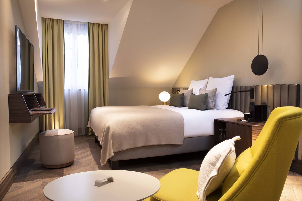 Una habitación de hotel moderna con una cama grande, una mesita de noche, una silla, una mesa redonda y un televisor.
