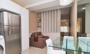A compact living space with a kitchenette, a glass dining table, a sofa, and a modern light fixture.