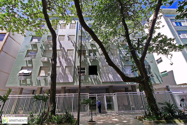 A multi-story building with balconies, a gated entrance, and surrounding greenery.