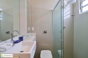 A modern bathroom with a glass shower enclosure, a white sink, and a toilet.