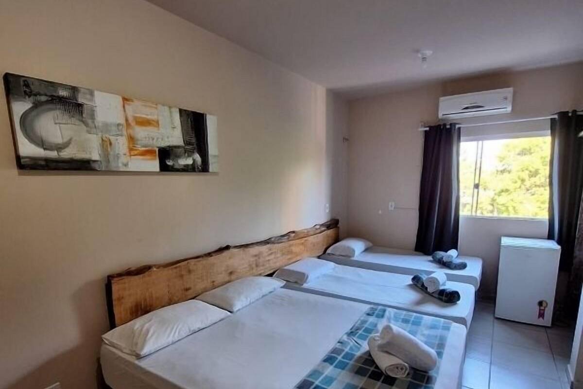 A hotel room with two beds, a small kitchenette, and a window with curtains.