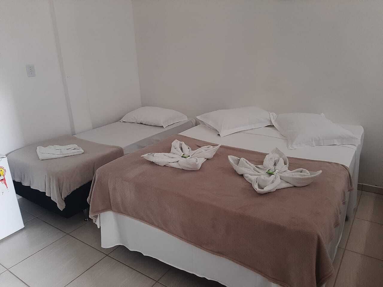 A hotel room with two beds, each with a brown blanket and white pillows. There is a small table with a white cloth and a bottle of water.