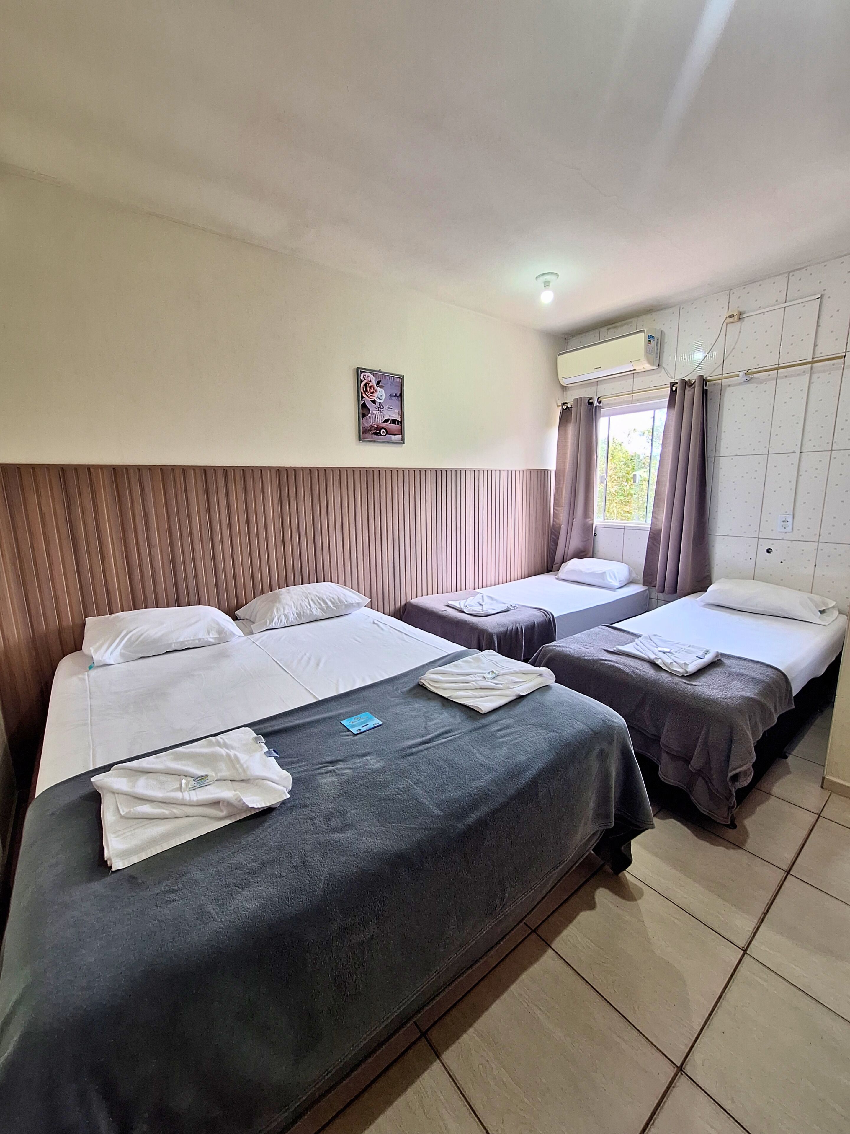 A hotel room with two beds, a wall-mounted air conditioner, and a window with curtains.