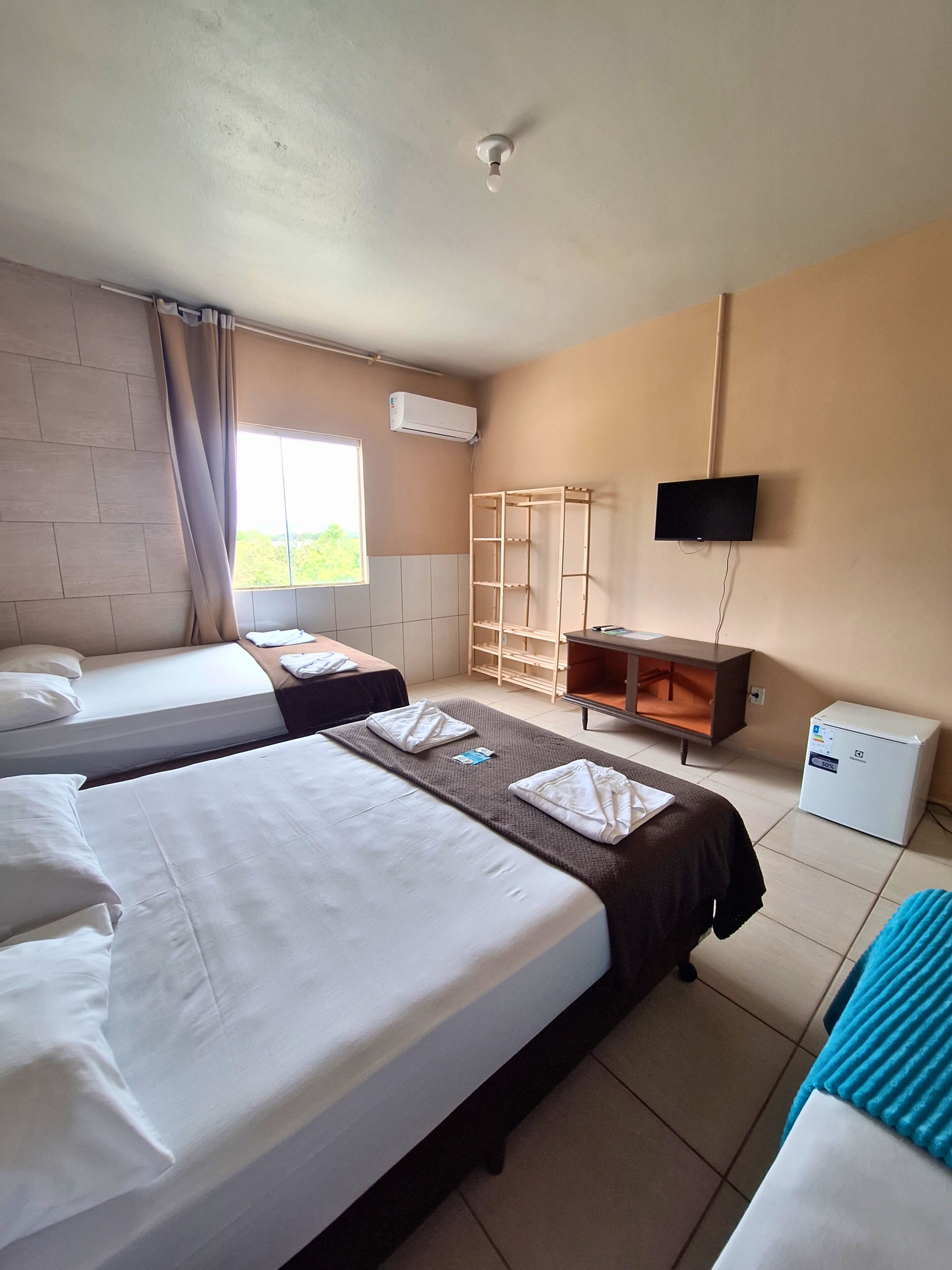 Quarto de hotel com duas camas, televisão presa à parede, um pequeno armário e um frigorífico.